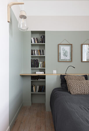 Détail d'une tête de lit avec bibliothèque intégrée, tablette en chêne et suspension design dans une décoration