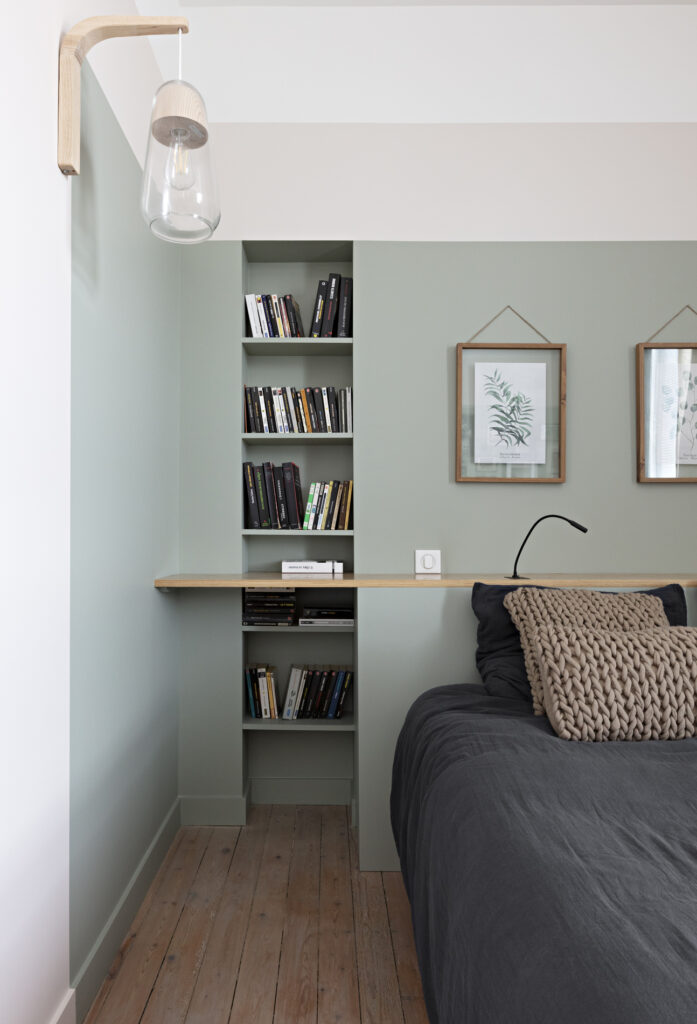 Détail d'une tête de lit avec bibliothèque intégrée, tablette en chêne et suspension design dans une décoration
