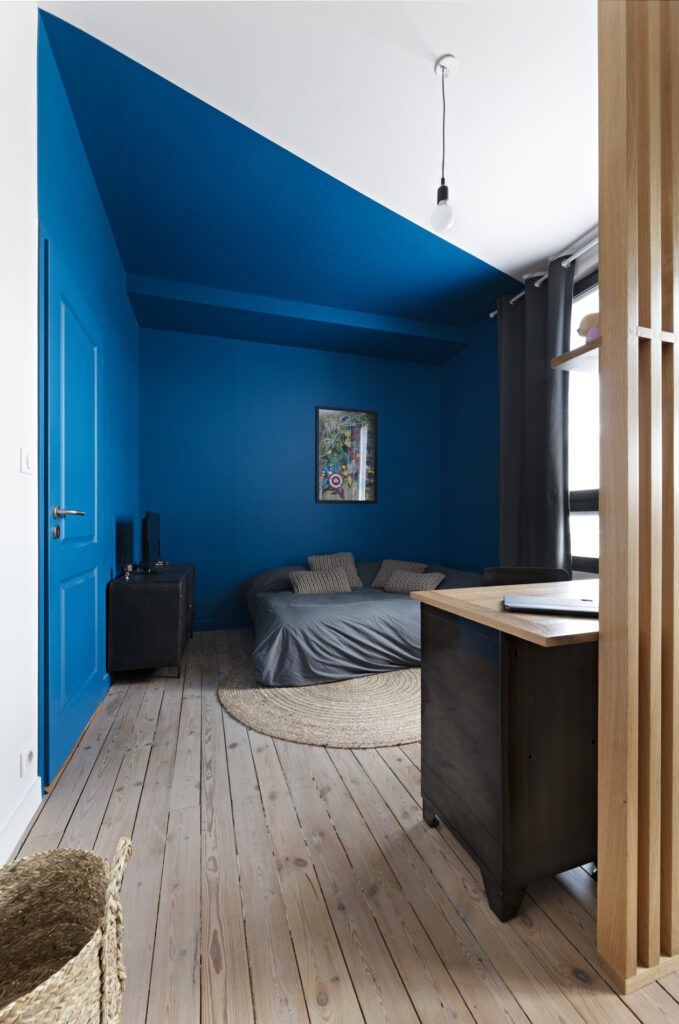 Chambre d'adolescent avec murs bleu intense, parquet ancien, bureau et claustra en chêne dans une maison décorée à Nantes.