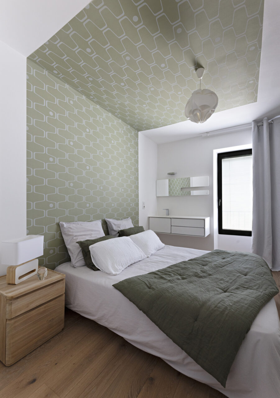 Chambre aux tons vert sauge avec papier peint graphique au plafond et mobilier blanc dans une décoration complète de maison à Nantes.