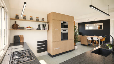 Cuisine en L rénovée à Sautron avec colonnes techniques, fours intégrés et plan de travail effet pierre