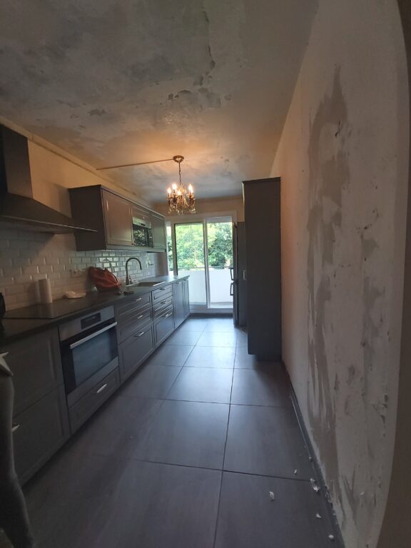 Cuisine contemporaine rénovée avec meubles gris, plan de travail noir et accès au balcon après une rénovation d'appartement après sinistre à Nantes.