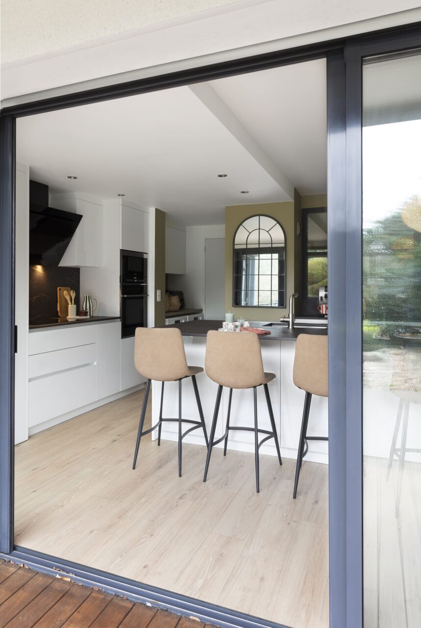 Vue de la cuisine rénovée avec îlot central XXL depuis la terrasse grâce à une grande baie vitrée à Sautron.