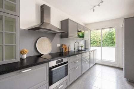 Cuisine contemporaine rénovée avec meubles gris, plan de travail noir et accès au balcon après une rénovation d'appartement après sinistre à Nantes.