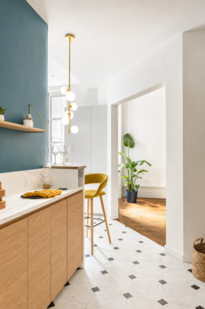 Cuisine contemporaine en chêne et mur bleu ouvrant sur le séjour dans une rénovation d'appartement ancien à Nantes.