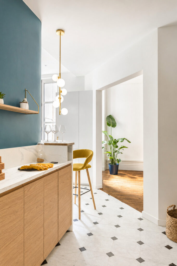 Cuisine contemporaine en chêne et mur bleu ouvrant sur le séjour dans une rénovation d'appartement ancien à Nantes.