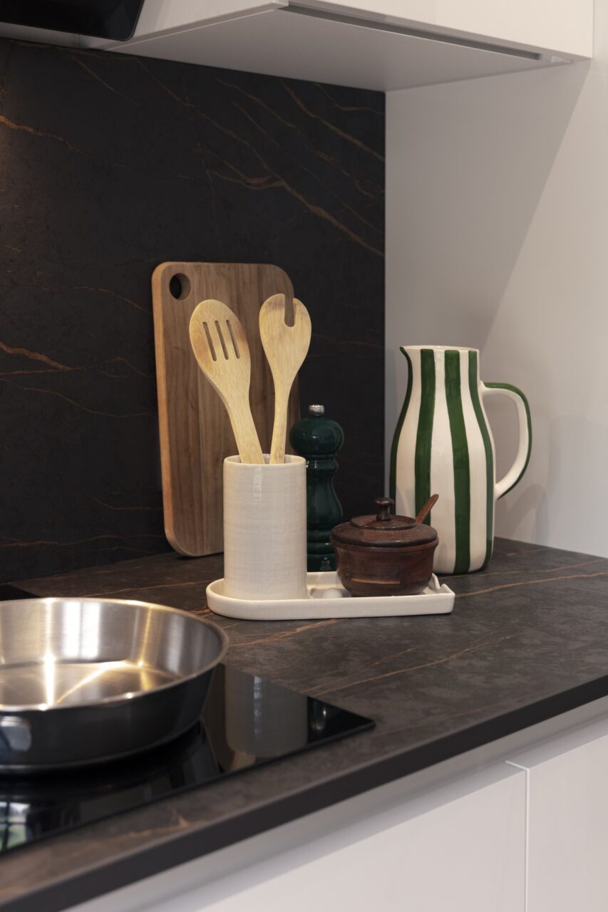 Plaque de cuisson, crédence effet pierre noire et plan de travail en céramique dans une rénovation de cuisine avec îlot central à Sautron.