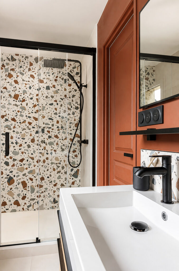 Perspective sur la douche avec paroi vitrée, robinetterie noire et meuble vasque en bois dans une salle d'eau optimisée à Vigneux-de-Bretagne.