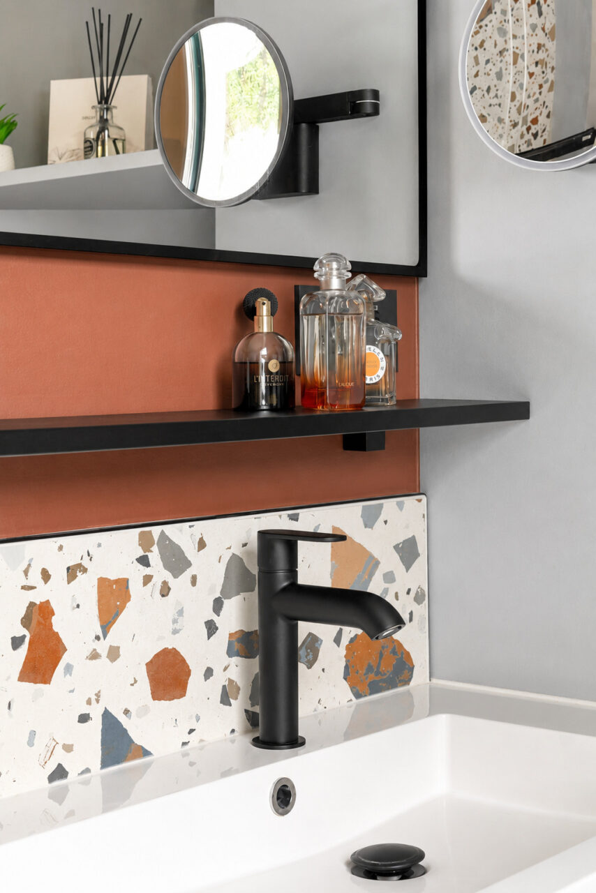Détail du meuble vasque suspendu avec robinetterie noire, crédence effet terrazzo et miroir dans une salle d'eau optimisée à Vigneux-de-Bretagne.