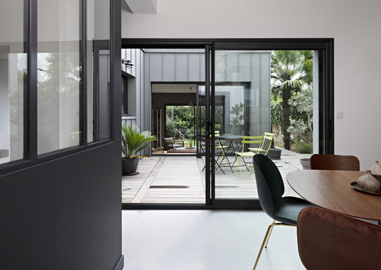 Vue de la salle à manger vers le patio et les grandes baies vitrées dans une décoration complète de maison aux sept ambiances à Nantes.