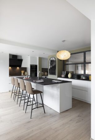 Vue générale de la cuisine rénovée avec grand îlot central, façades blanches et plan de travail noir à Sautron.