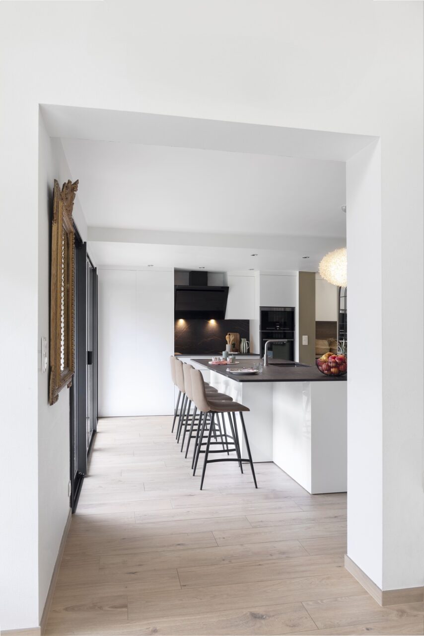 Cuisine rénovée avec îlot central XXL blanc et plan de travail noir, vue depuis l'entrée de la maison à Sautron.