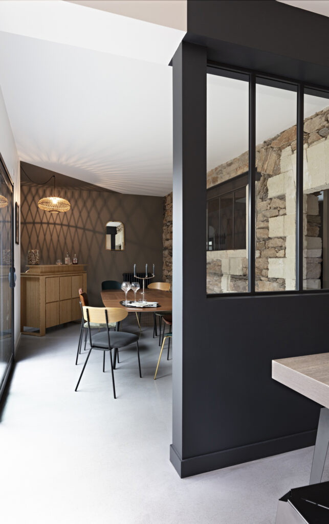 Salle à manger chaleureuse avec verrière intérieure, pierre apparente et décoration complète d'une maison aux sept ambiances à Nantes.