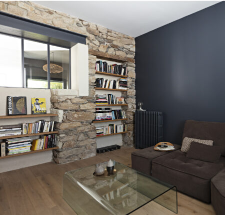 Salon contemporain avec bibliothèque intégrée dans un mur en pierre, parquet en chêne et mobilier sur mesure dans une décoration complète de maison à Nantes.