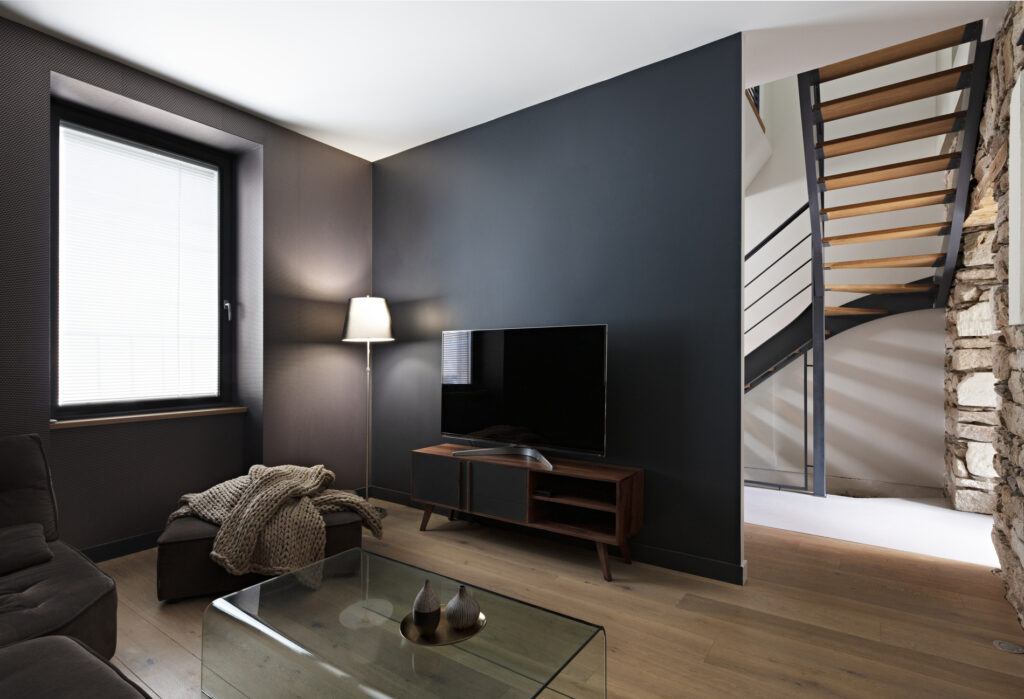 Salon TV contemporain avec mur noir, escalier métal et bois, dans une décoration complète de maison aux sept ambiances à Nantes.