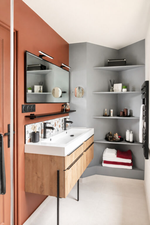 Salle d'eau optimisée à Vigneux-de-Bretagne comprenant un meuble double vasque suspendu, des étagères d'angle sur mesure et une décoration aux teintes terracotta et gris.