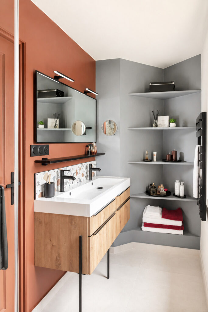 Salle d'eau optimisée à Vigneux-de-Bretagne comprenant un meuble double vasque suspendu, des étagères d'angle sur mesure et une décoration aux teintes terracotta et gris.